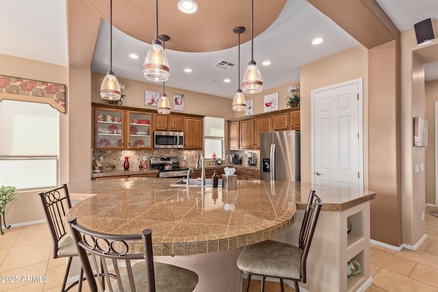 kitchen featuring tasteful backsplash, a large island with sink, light tile patterned flooring, appliances with stainless steel finishes, and a breakfast bar area