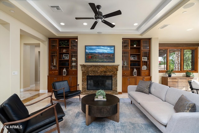 living room with a raised ceiling, ceiling fan, and a fireplace