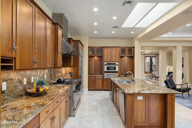 kitchen featuring a spacious island, sink, a skylight, appliances with stainless steel finishes, and light stone counters