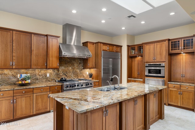 kitchen featuring sink, wall chimney range hood, stainless steel appliances, and a kitchen island with sink