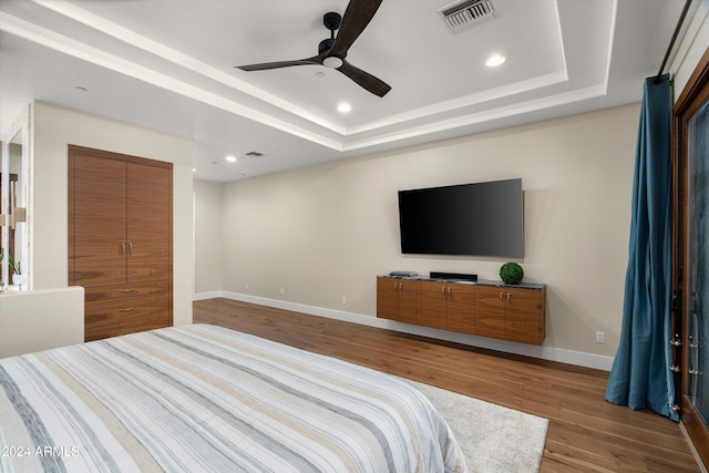 bedroom with wood-type flooring, a closet, a raised ceiling, and ceiling fan