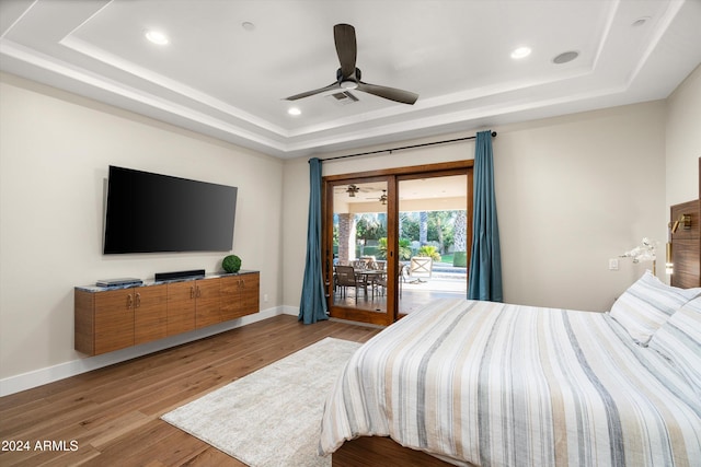 bedroom featuring light wood-type flooring, access to outside, a raised ceiling, and ceiling fan