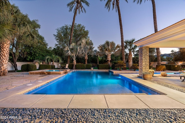 pool at dusk featuring an in ground hot tub and a patio