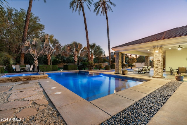 pool at dusk featuring a patio area and an in ground hot tub