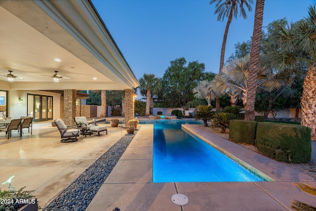 pool at dusk with french doors, a patio, and ceiling fan