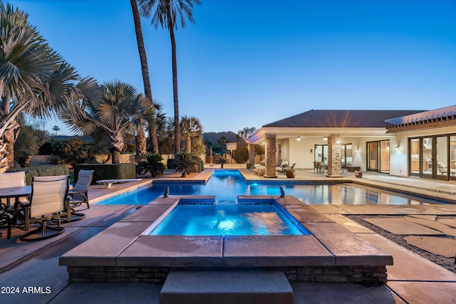 pool at dusk with an in ground hot tub and a patio