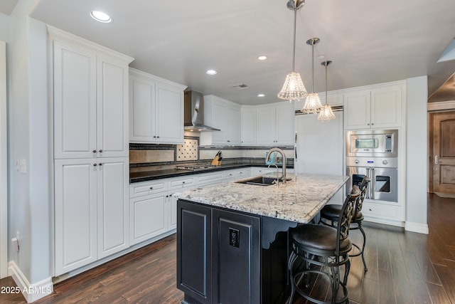 kitchen featuring built in appliances, white cabinetry, wall chimney exhaust hood, and a sink