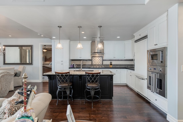 kitchen with built in appliances, dark wood-style flooring, wall chimney exhaust hood, and a sink