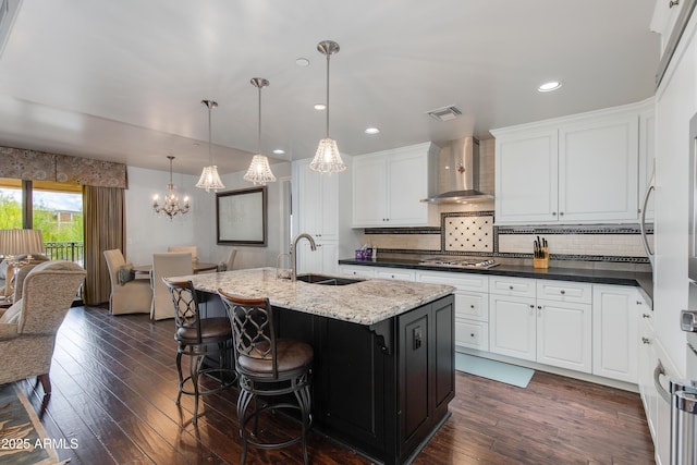 kitchen with visible vents, a sink, dark wood-style floors, white cabinetry, and wall chimney range hood