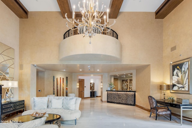 living area featuring a notable chandelier, beam ceiling, a high ceiling, and baseboards