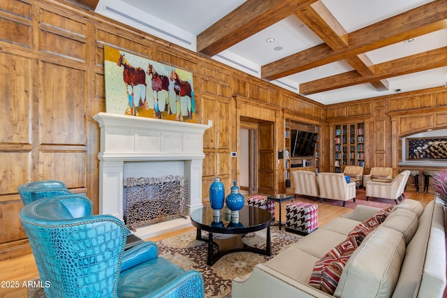 living room featuring beamed ceiling, a fireplace with raised hearth, coffered ceiling, wood finished floors, and wooden walls