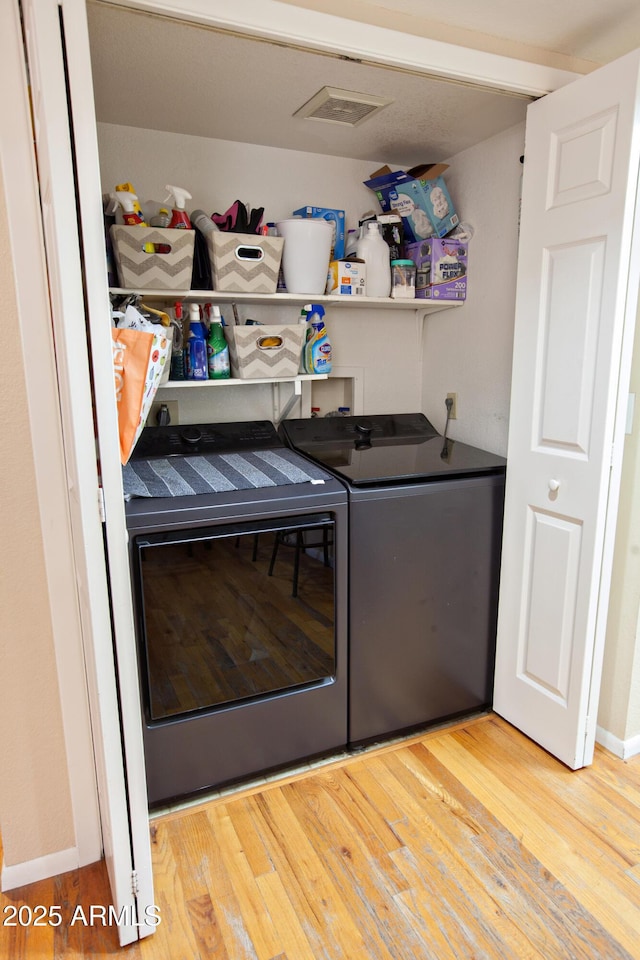 clothes washing area with washer and clothes dryer and light hardwood / wood-style flooring