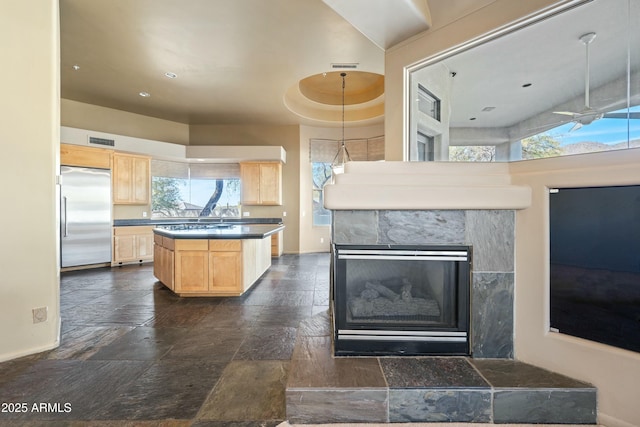 kitchen featuring stainless steel built in refrigerator, light brown cabinetry, a kitchen island, pendant lighting, and a fireplace