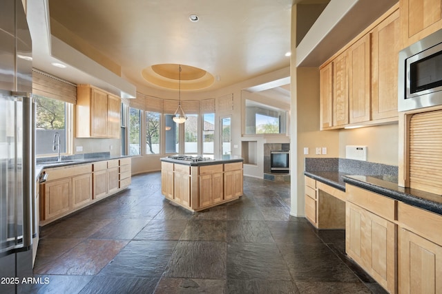 kitchen featuring a raised ceiling, sink, light brown cabinets, and decorative light fixtures