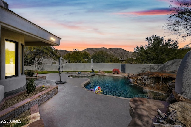 pool at dusk featuring a mountain view, a patio area, and pool water feature