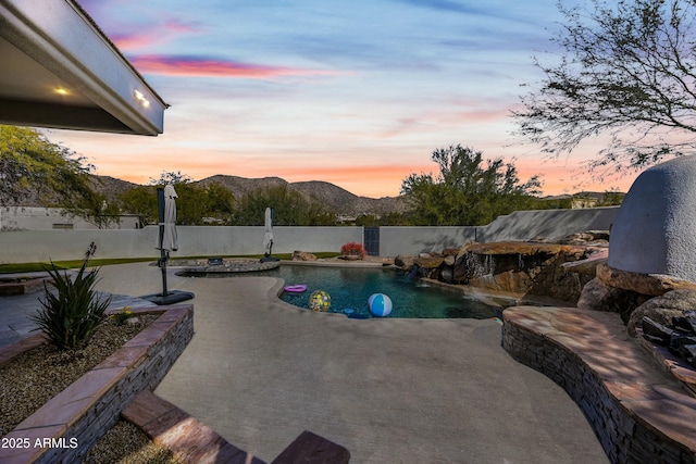 pool at dusk featuring pool water feature, a mountain view, and a patio