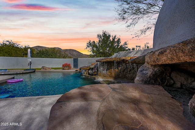 pool at dusk with pool water feature and a mountain view