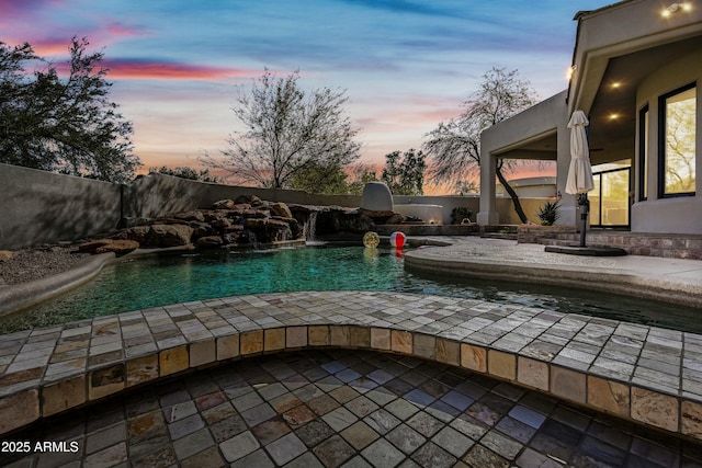 pool at dusk featuring pool water feature and a patio area