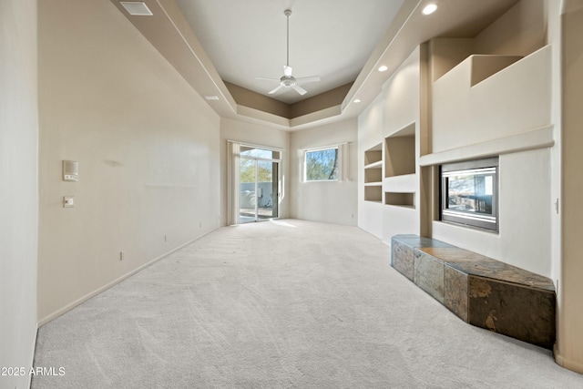 unfurnished living room featuring a raised ceiling, light colored carpet, and ceiling fan