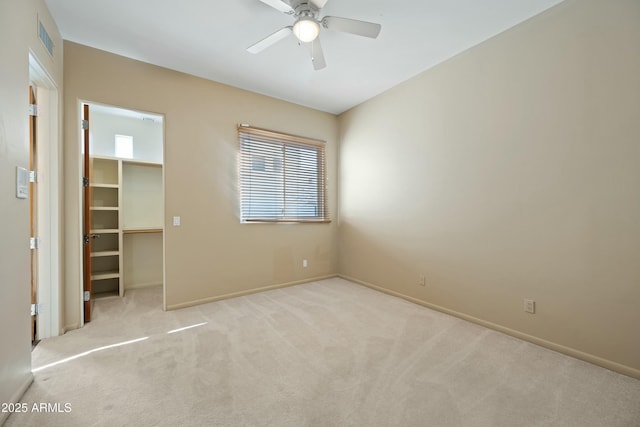 unfurnished bedroom featuring a walk in closet, light carpet, ceiling fan, and a closet