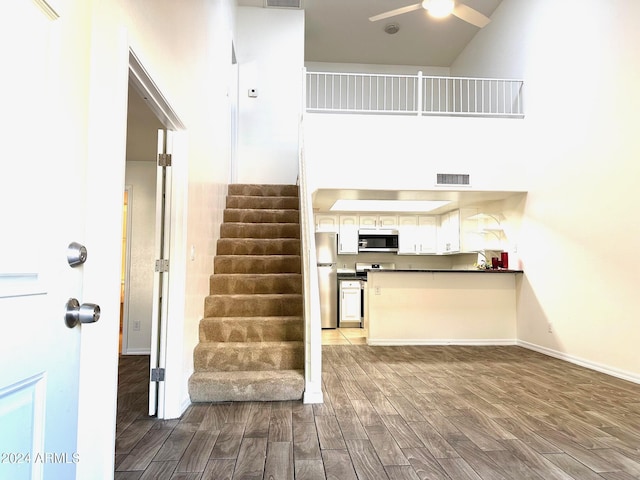 kitchen with white cabinets, hardwood / wood-style flooring, ceiling fan, a towering ceiling, and stainless steel appliances