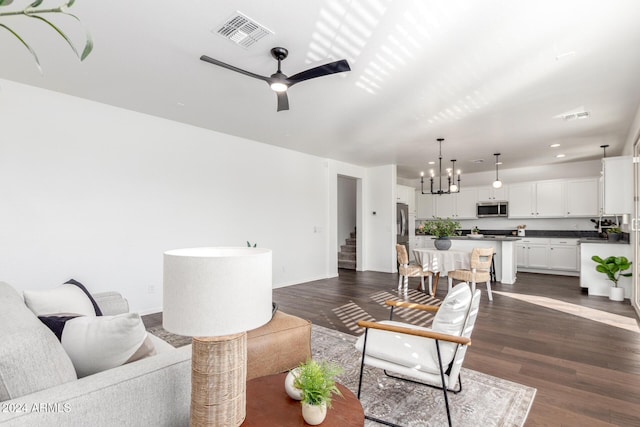 living room with ceiling fan with notable chandelier and dark hardwood / wood-style floors