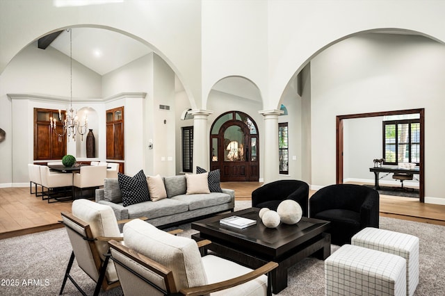 living room with a towering ceiling, an inviting chandelier, light hardwood / wood-style floors, and decorative columns