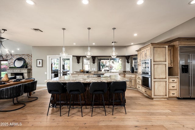 kitchen with light stone countertops, light hardwood / wood-style floors, hanging light fixtures, and built in appliances