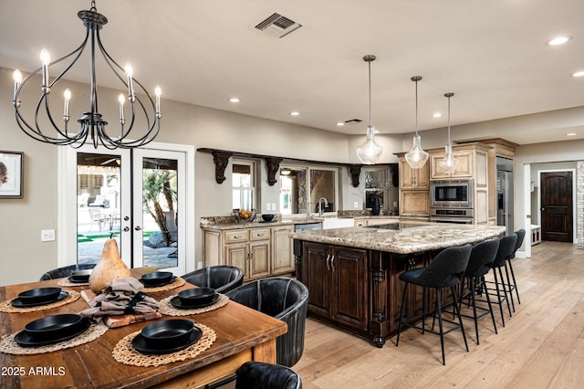 kitchen featuring a center island, stainless steel appliances, hanging light fixtures, a chandelier, and light stone counters