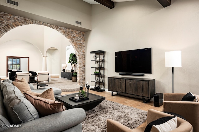 living room with a towering ceiling, beamed ceiling, decorative columns, and light hardwood / wood-style flooring