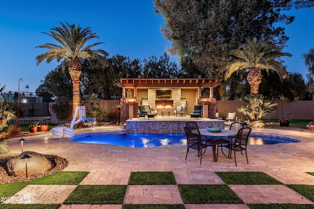 pool at dusk with pool water feature, an outdoor fireplace, and a patio area