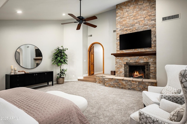 carpeted bedroom with a towering ceiling, ceiling fan, and a stone fireplace