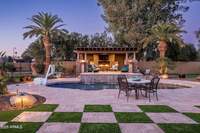 patio terrace at dusk featuring pool water feature, an outdoor fireplace, and a fenced in pool