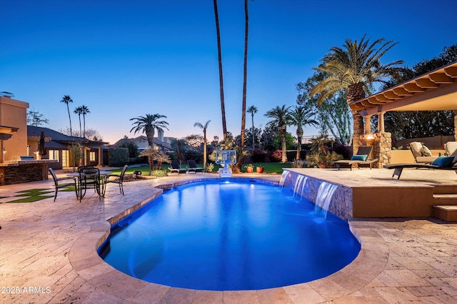 pool at dusk with a patio area and pool water feature