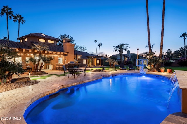 pool at dusk featuring a patio area and pool water feature