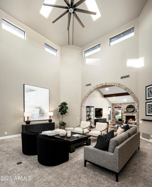 living room featuring ceiling fan, a towering ceiling, carpet floors, and a stone fireplace