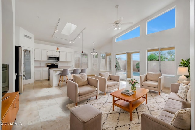 tiled living room with ceiling fan, track lighting, high vaulted ceiling, and a skylight