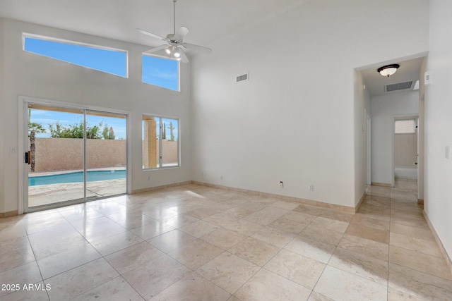 empty room featuring ceiling fan, light tile patterned floors, and a high ceiling