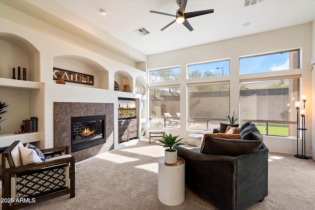 living room featuring light colored carpet, a fireplace, built in features, and ceiling fan