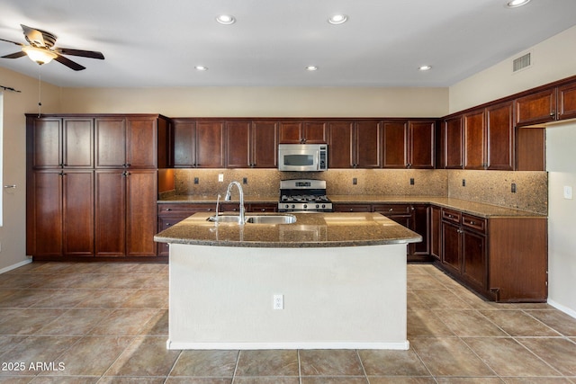 kitchen with a center island with sink, appliances with stainless steel finishes, stone countertops, and sink