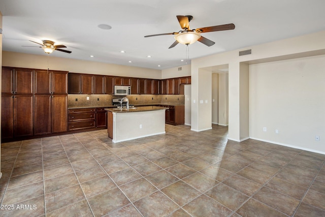 kitchen with sink, ceiling fan, tile patterned flooring, tasteful backsplash, and an island with sink