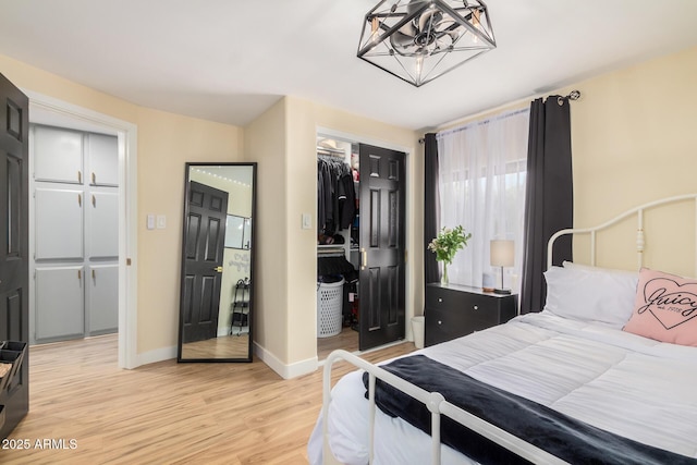 bedroom with light wood-type flooring, baseboards, a chandelier, and a closet