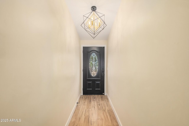 doorway with light wood-type flooring, an inviting chandelier, and baseboards