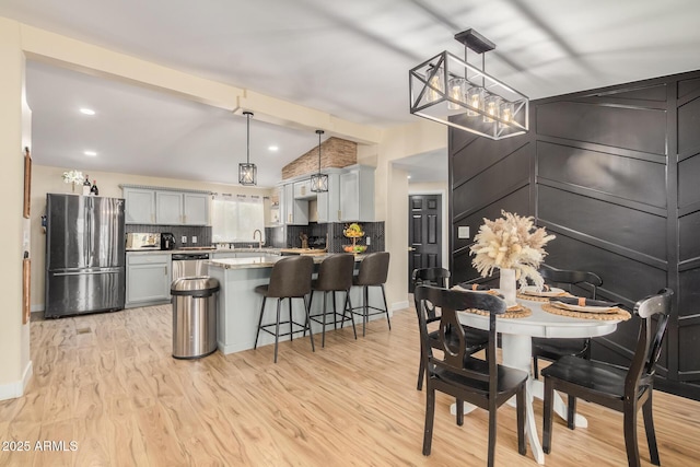 kitchen with a breakfast bar, stainless steel appliances, lofted ceiling with beams, decorative backsplash, and light wood-type flooring