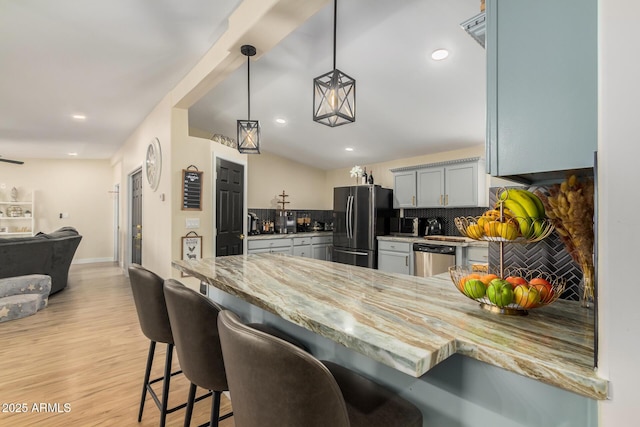 kitchen with kitchen peninsula, appliances with stainless steel finishes, a kitchen bar, tasteful backsplash, and decorative light fixtures