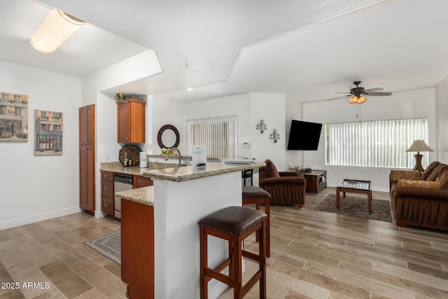 kitchen with brown cabinets, a peninsula, dishwasher, open floor plan, and a kitchen bar