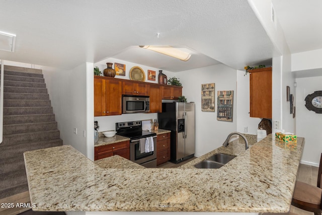 kitchen with light stone countertops, a peninsula, a sink, appliances with stainless steel finishes, and a kitchen breakfast bar