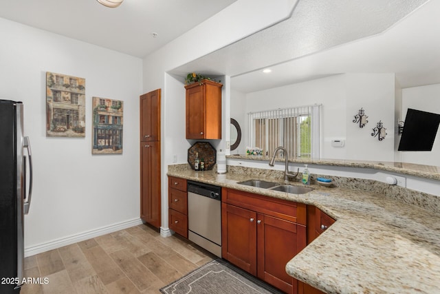 kitchen with light wood finished floors, appliances with stainless steel finishes, light stone counters, and a sink