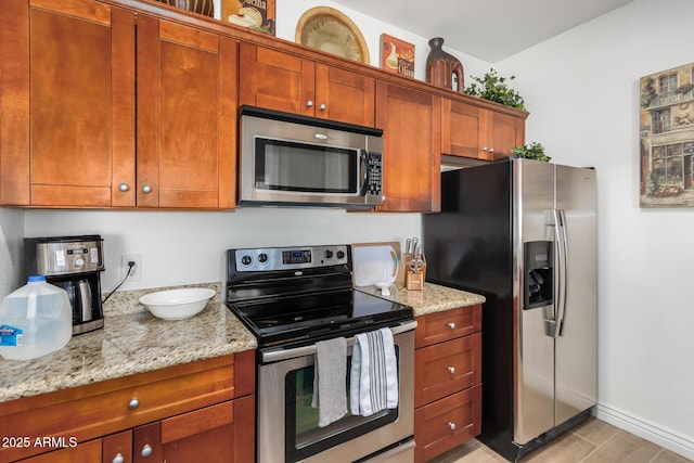 kitchen featuring brown cabinetry, light stone countertops, baseboards, and appliances with stainless steel finishes