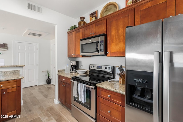 kitchen with stainless steel appliances, light stone countertops, visible vents, and brown cabinetry